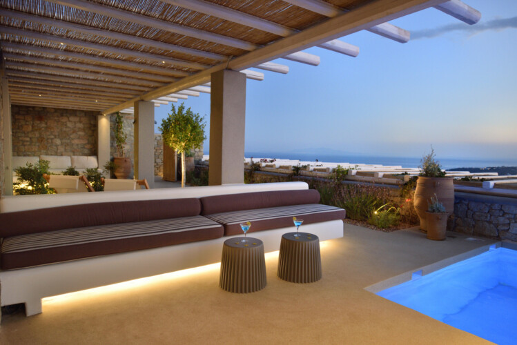 sunset with drinks at the outdoor sitting area from villa ammolite in mykonos, swimming pool with lights and a gorgeous terrace
